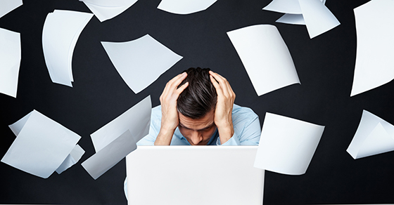 Stressed business man sitting by laptop while papers falling over him